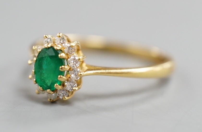 A modern 18ct gold, oval cut emerald and diamond chip set oval cluster ring, size N/O, gross weight 2.5 grams